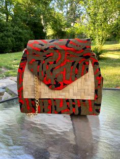 "Stand out with this medium-sized, unique handmade red and camo colored African waxprint and straw handbag! It also comes with a matching, foldable hand fan made of cloth and straw. This bag can be worn as a shoulder or crossbody purse. The strap is a gold chain and it has a magnetic clasp to close. The purse has a black lining and a small interior pocket. Whenever you want to make a stunning fashion statement, bright colors and bold patterns will be your choice. This handmade Straw Clutch Purse Tweed Handbag, African Bag, African Paintings, Straw Clutch, Straw Handbags, Handmade African, Camo Colors, Magnetic Clasp, Black Canvas