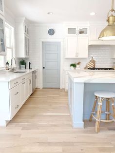 a white kitchen with an island and stools in the center, along with two gold pendant lights