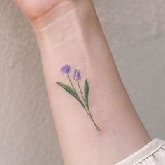 a woman's wrist with a small purple flower tattoo on the left side of her arm