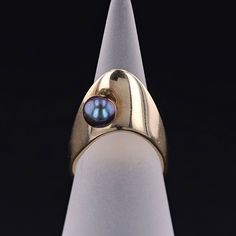 Legend has it that Oro, a Polynesian god of fertility and peace, gifted a black pearl to his beloved.  This has lead to black pearls symbolizing independence, strength, and love. This vintage ring (circa 1980-1990) features a black pearl set atop a modernist, 14k gold mounting.   The ring is currently a size 5 and it weighs 6.5 grams.  The ring can be re-sized a bit free of charge.   We have many other fantastic offerings of fine jewelry posted on our Etsy store, so please consider browsing our Modernist Jewelry Pearl, God Of Fertility, Black Pearl Ring, Black Peas, Modernist Ring, Black Pearls, Jewelry Post, Pearl Set, Antique Diamond