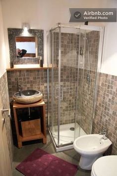 a bathroom with a toilet, sink and shower stall in the corner next to a rug on the floor