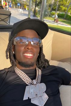 a man wearing sunglasses and a hat sitting on a couch with his arms behind him