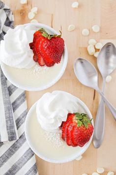 two plates with strawberries and whipped cream on them next to spoons, napkins and utensils