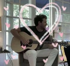 a man sitting in a chair playing a guitar with hearts drawn on the wall behind him