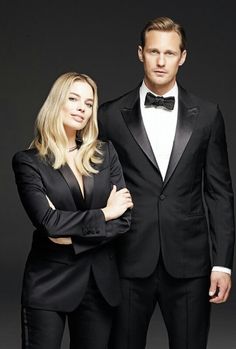 a man in a tuxedo standing next to a woman wearing a black suit