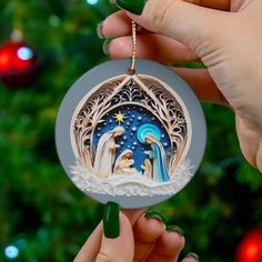 a hand holding a christmas ornament with an image of the birth of jesus