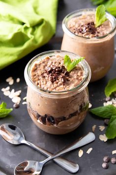 two small jars filled with chocolate pudding and topped with mint sprinkles on a table