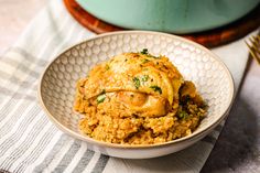 a white bowl filled with chicken and rice on top of a striped table cloth next to a green pot