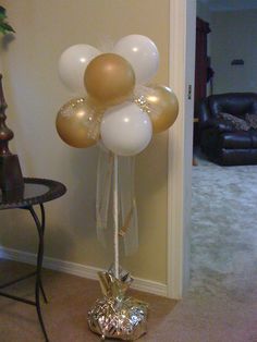 a bunch of balloons that are in the air near a table and chair with a vase on it