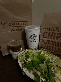 a plate of salad next to two bags of chips and a cup of coffee on a table