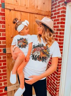 a woman holding a small child in her arms while wearing matching tshirt and hat