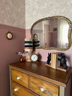 a dresser with a mirror, clock and other items on it in front of a pink wall