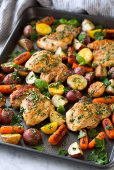 chicken, potatoes and carrots on a baking sheet with herbs sprinkled on top