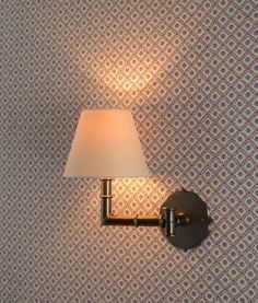 a lamp on a wall in a room with patterned wallpaper and a white shade