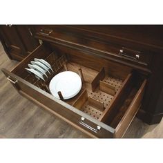 an open drawer with plates and utensils in it on top of a wooden floor