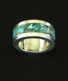 This glamorous Turquoise and Sterling Silver Ring was handcrafted by Nevada Silversmith Jim Daggett. The Ring Band was made from melted Sterling Silver, which was rolled to the desired thickness and then cut, shaped and soldered into a Band. A Sterling Rim was applied at the top and bottom of the Ring, creating a channel in the center. This channel has been inlaid with Turquoise Chip, creating a mosaic of shapes in medium and light-blue hues. The Rolled Sterling is thicker than regular 20 gauge Artisan Turquoise Jewelry With Polished Finish, Unique Turquoise Jewelry With Polished Finish, Unique Turquoise Rings With Polished Finish, Turquoise Rings With Polished Finish, Artisan Rings With Inlay For Anniversary, Turquoise Polished Ring, Turquoise Ring With Patina, Artisan Multi-stone Turquoise Ring, Turquoise Rings With Polished Finish For Anniversary