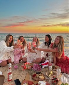 a group of women sitting on top of a wooden floor next to the ocean at sunset