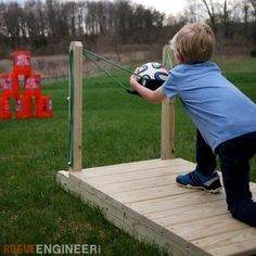 a young boy is playing with a soccer ball on a wooden platform in the grass