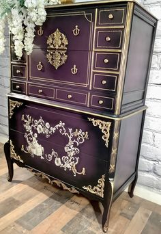 a purple and gold dresser sitting on top of a hard wood floor next to a vase with flowers