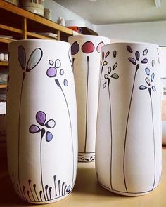 three white vases sitting on top of a wooden table next to each other with flowers painted on them