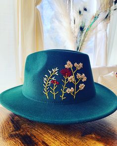 a green hat sitting on top of a wooden table next to a vase with flowers