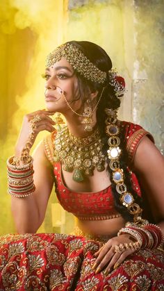 a woman in a red and gold outfit with jewelry on her head, sitting down