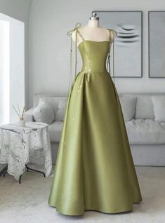 Knockout sophistication meets earthy grace in this exquisite prom dress. Its muted green shade stands out with a unique understated beauty, evoking the calm of woodland scenes. The fitted bodice, held by slender, lace-up straps, introduces a contemporary twist to the classic gown silhouette. The skirt, cut from lustrous satin, flows in generous folds, adding a regal touch to the dressoverall simplicity. Subtle floral embroidery adds a whisper of detail, suggesting a narrative of elegance and poise. This gown is the perfect choice for the prom-goer who wishes to exude a serene confidence, wrapped in a design thatboth grounding and ethereal. Wrap Prom Dress, Olive Green Prom Dress, Green Satin Prom Dress, Formal Dresses Plus Size, Ethereal Gowns, Classic Gown, Gown Silhouette, Princess Prom Dresses, Winter Formal Dresses