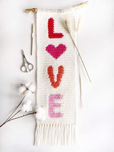 a knitted love banner with scissors, cotton flowers and needles on a white surface