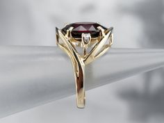 This is a stunning cocktail mounting crafted from shining yellow gold! The ring is really all about the center stone, and the simple styling and accent diamonds create the perfect stage! Deep, crimson red, this garnet is the color of a fine cabernet, poured in a golden glass.Metal: 14K Yellow GoldGem: Garnet 6.50 CaratsGem Measurements: 13.2 x 10.6 mm, OvalAccents: 2 Diamonds totaling .10 Carats, I1 in Clarity, G in ColorRing Size: 6.75Marks: "14KP" Stamped on the inside band Formal Garnet Burgundy Ring, Formal Burgundy Garnet Ring, Elegant Garnet Ring With Prong Setting, Elegant Burgundy Garnet Rings, Elegant Ruby Ring With Diamond And Polished Finish, Elegant Garnet Ring With Center Stone, Elegant Ruby Ring With Polished Finish, Formal Ruby Ring With Gemstone Accents, Elegant Garnet Round Cut Rings