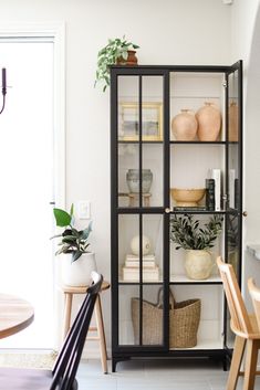 an open bookcase with plants and other items on it in a dining room area