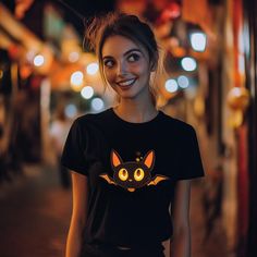 Light up the night with our Cute Bat Halloween T-Shirt! Featuring an adorable bat design with glowing eyes, this spooky-cute tee is perfect for Halloween festivities or casual fall nights. Whether you're headed to a party or just enjoying the season, this unisex shirt brings a fun and playful touch to your look. Soft & Comfortable: Made from premium, breathable cotton for a cozy feel. Glow-in-the-Dark Design: The bat's eyes light up, making you stand out in low light. Unisex Fit: Available in multiple sizes, perfect for everyone. Great for Halloween: Ideal for parties, trick-or-treating, or as a fun gift. Get ready to turn heads and spread spooky vibes with this unique Halloween T-shirt! Black Graphic Tee With Glow In The Dark Details, Black Short Sleeve Glow In The Dark T-shirt, Glow In The Dark Short Sleeve Graphic Tee, Glow In The Dark Graphic Tee With Short Sleeve, Casual Black Glow In The Dark Top, Halloween Glow In The Dark Black Top, Black Glow In The Dark Crew Neck Top, Bat Eyes, Bat Design