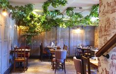 the interior of a restaurant with wooden tables and chairs covered in ivy hanging from the ceiling