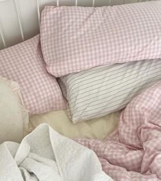 an unmade bed with pink gingham sheets and pillows