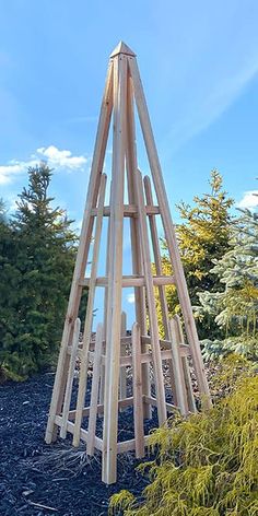 a tall wooden tower sitting on top of a gravel field next to trees and bushes