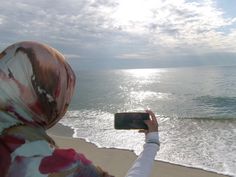 a woman taking a photo on the beach with her cell phone