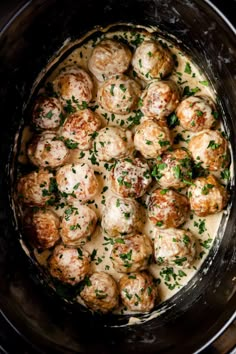 a crock pot filled with meatballs covered in gravy and garnished with parsley