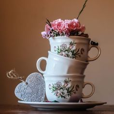 three tea cups stacked on top of each other with pink flowers in them and a heart shaped cookie