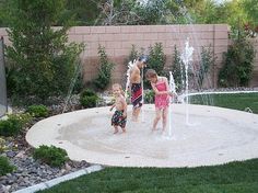 two young children playing in a water sprinkler at the back yard pool