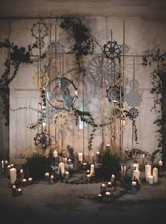 an arrangement of candles and greenery is displayed in front of a wall with gears on it