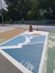 a woman sitting on the ground in front of a painted basketball court