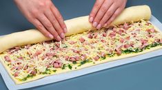 a person making a pizza with ham and cheese on it's side, while holding a rolling pin in their left hand