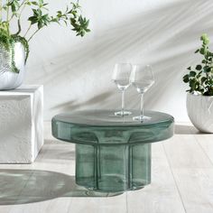 two wine glasses sitting on top of a glass table next to potted plants and vases