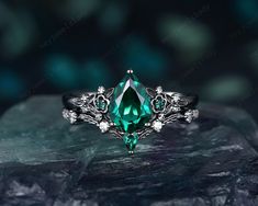 an emerald colored ring with white diamonds and leaves around it on top of a rock