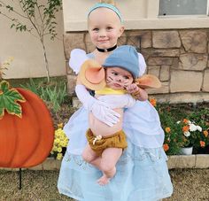 two children dressed up as disney characters in front of a pumpkin and flower garden area