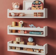 two white shelves with toys on them against a pink wall in a child's room