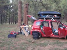 a red car parked in the woods with its door open and luggage on top of it