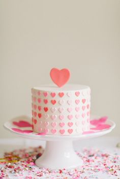 a white cake with pink hearts on top and sprinkles all around it