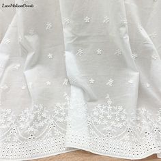 an embroidered white curtain with flowers on it and lace trimming around the edges, sitting on a wooden floor