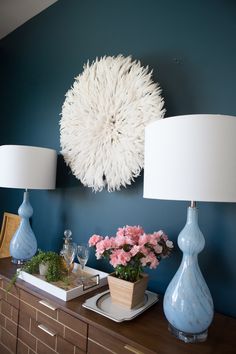 two lamps are sitting on a dresser in front of a blue wall