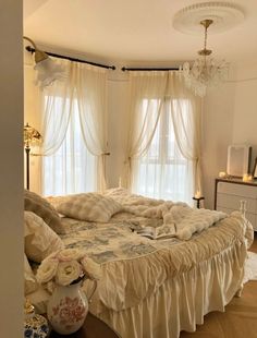 a large bed sitting next to a window with curtains on top of it and a chandelier hanging from the ceiling